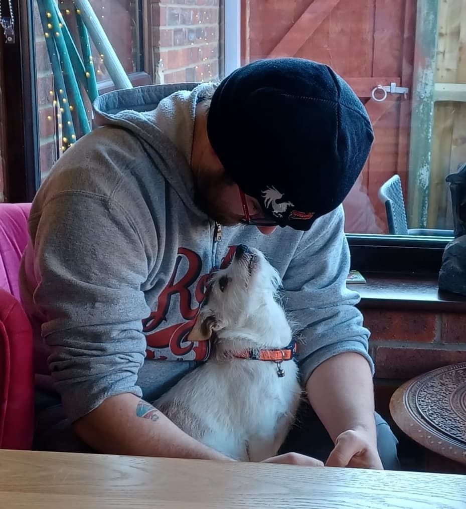 Picture of a Jack Russell sat on their owner's lap. The dog is staring up and the owner is looking down at them.